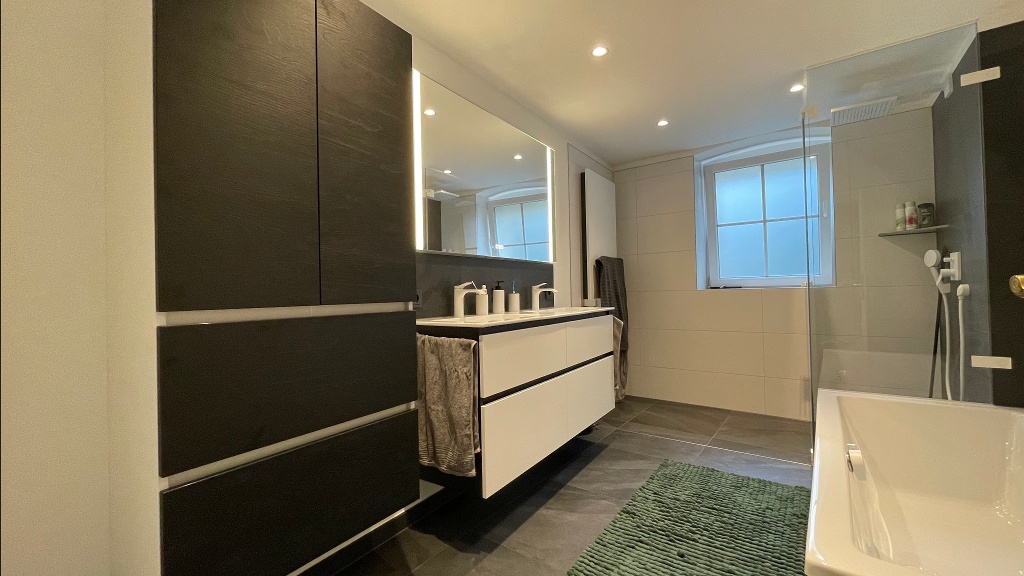 Für die Kunden war es von Bedeutung, eine große, bodengleiche Dusche zu erhalten, und dieses Vorhaben haben wir erfolgreich umgesetzt. Eine besondere Note im Badezimmer kam von der Auswahl der Armaturen von Hansgrohe! Das weiße Design fügt sich nahtlos in das Konzept ein, und die Serie Vivenis erfüllte alle Wünsche. Dabei wurde an jedes Detail gedacht, einschließlich des passenden Farbsets für die Badewanne. 

Die Waschtischanlage und der Hochschrank von Primabad erwiesen sich als wahre Stauraumwunder. Dadurch konnte die Kundin alles und noch mehr im neuen Bad unterbringen. Der Leuchtspiegel von Frasco rundete das Gesamtbild perfekt ab. Die Emotionsbeleuchtung – mit der Möglichkeit zwischen Warm- und Kaltlicht sowie einer Dimmfunktion – erwies sich als äußerst praktisches Hilfsmittel im Bad.